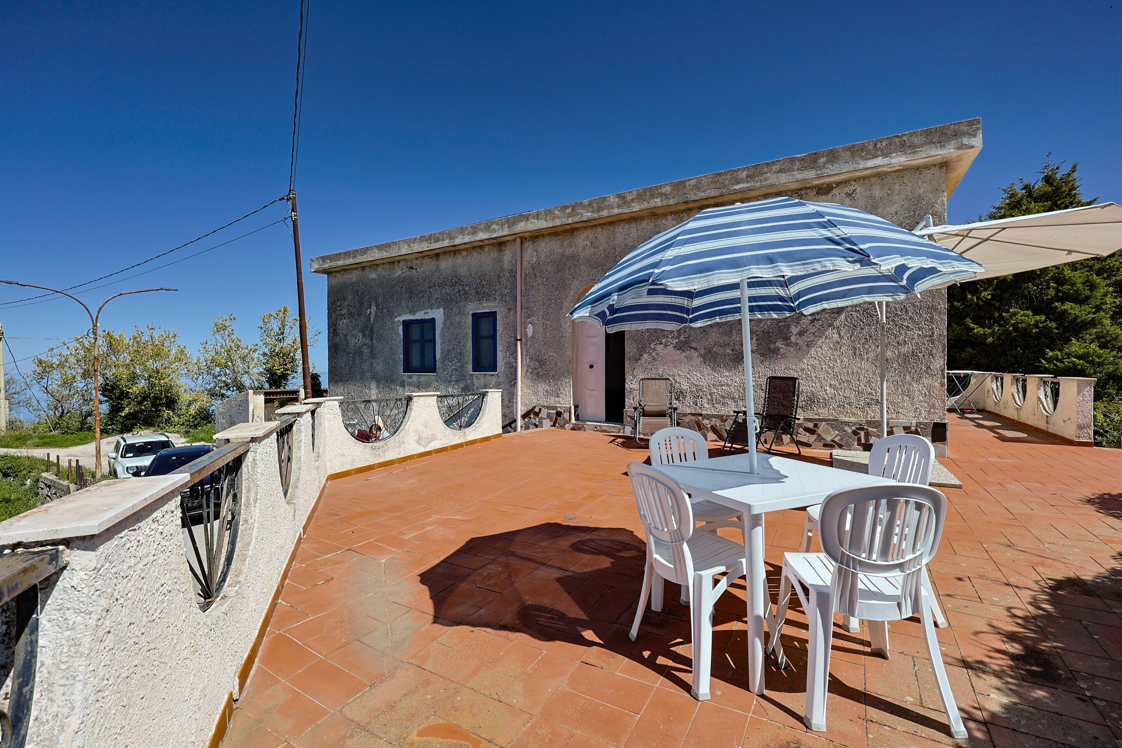 Eine Terrasse mit Tisch und Stühlen, einem gestreiften Sonnenschirm und einem Gebäude mit einer Stein-Fassade.