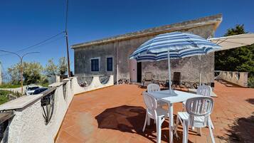 Eine Terrasse mit Tisch und Stühlen, einem gestreiften Sonnenschirm und einem Gebäude mit einer Stein-Fassade.