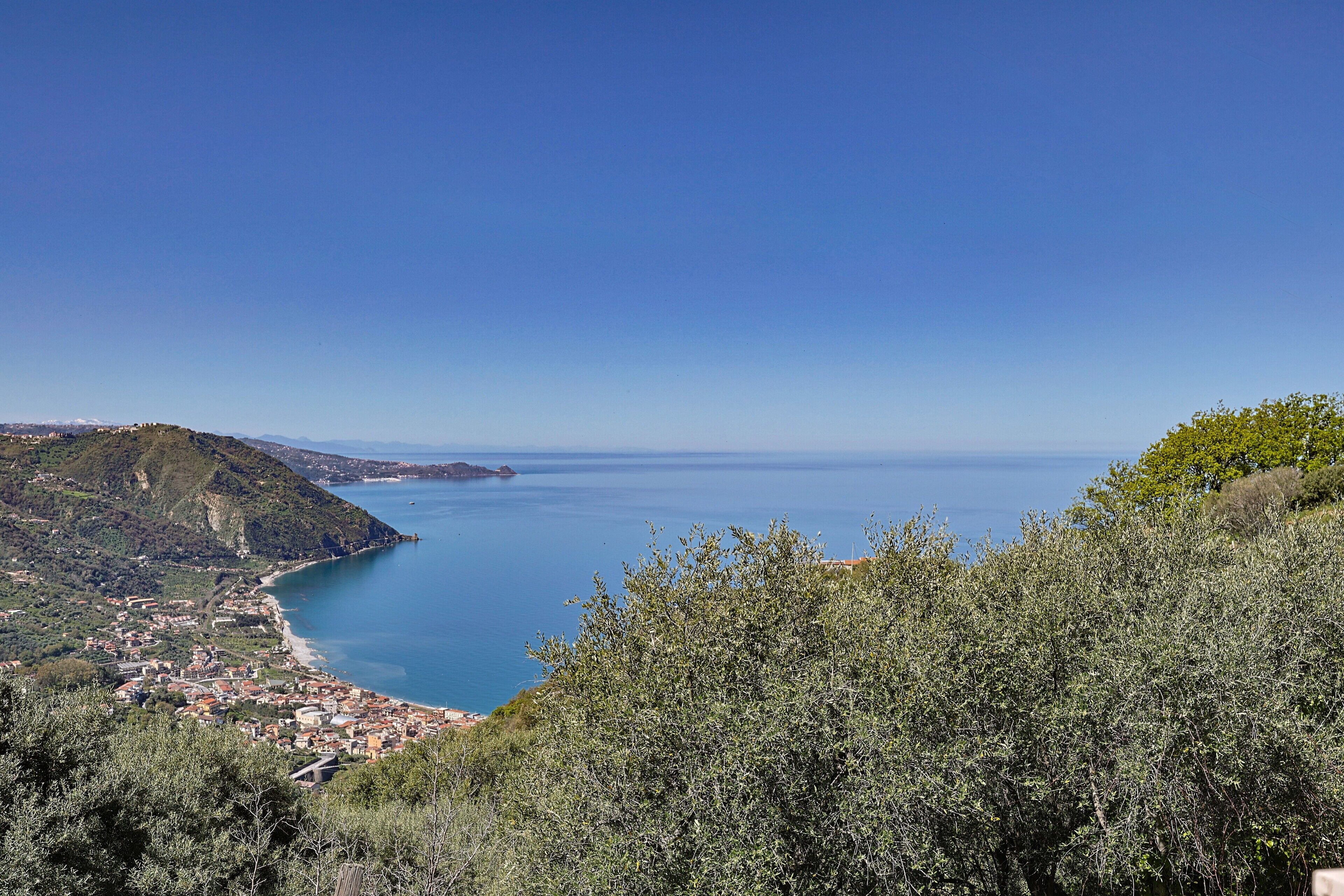 A coastal town with a view of the sea, surrounded by hills and dense vegetation.