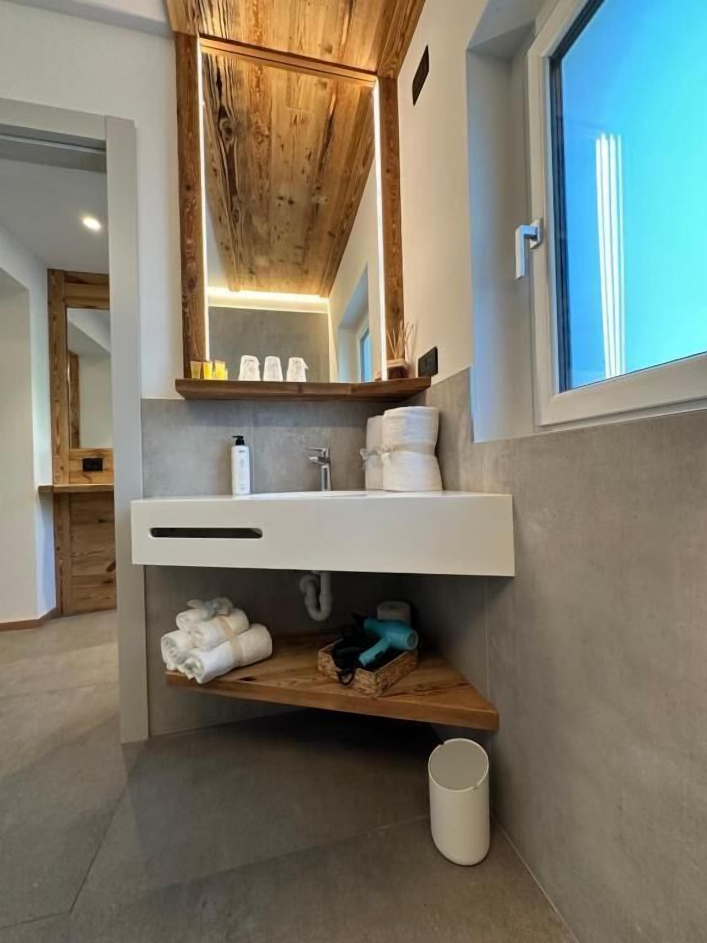 Een moderne badkamer met een houten plafond, een grote spiegel, een witte wastafel en een raam.