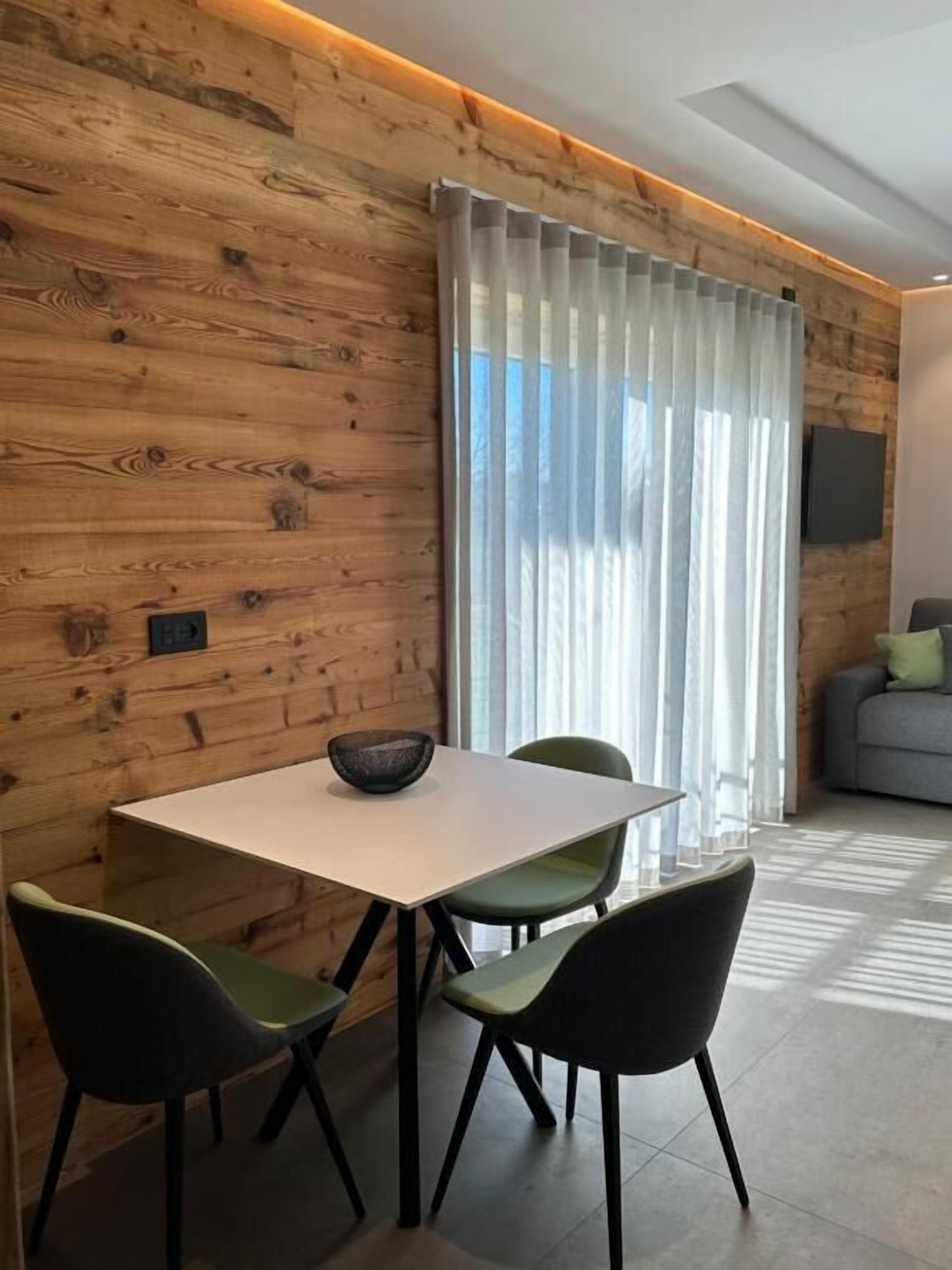 A modern dining area with a wooden wall, a white table, and green chairs.