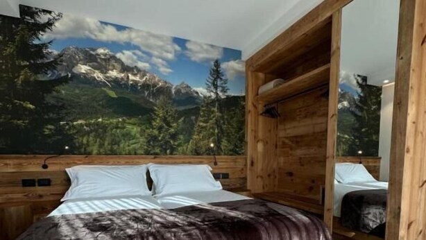A bedroom with a bed, wooden headboard, and a mural of a mountain landscape. - ORIGINI HOLIDAYS  (Sedico)