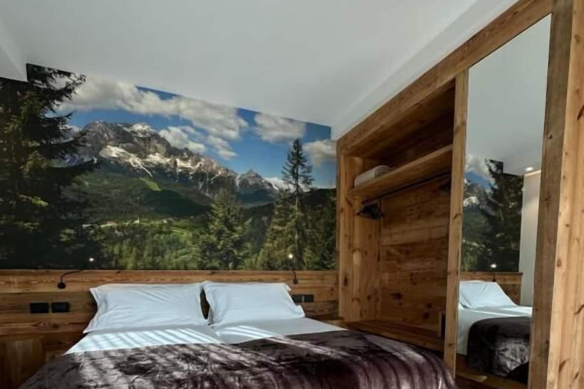 A bedroom with a bed, wooden headboard, and a mural of a mountain landscape.