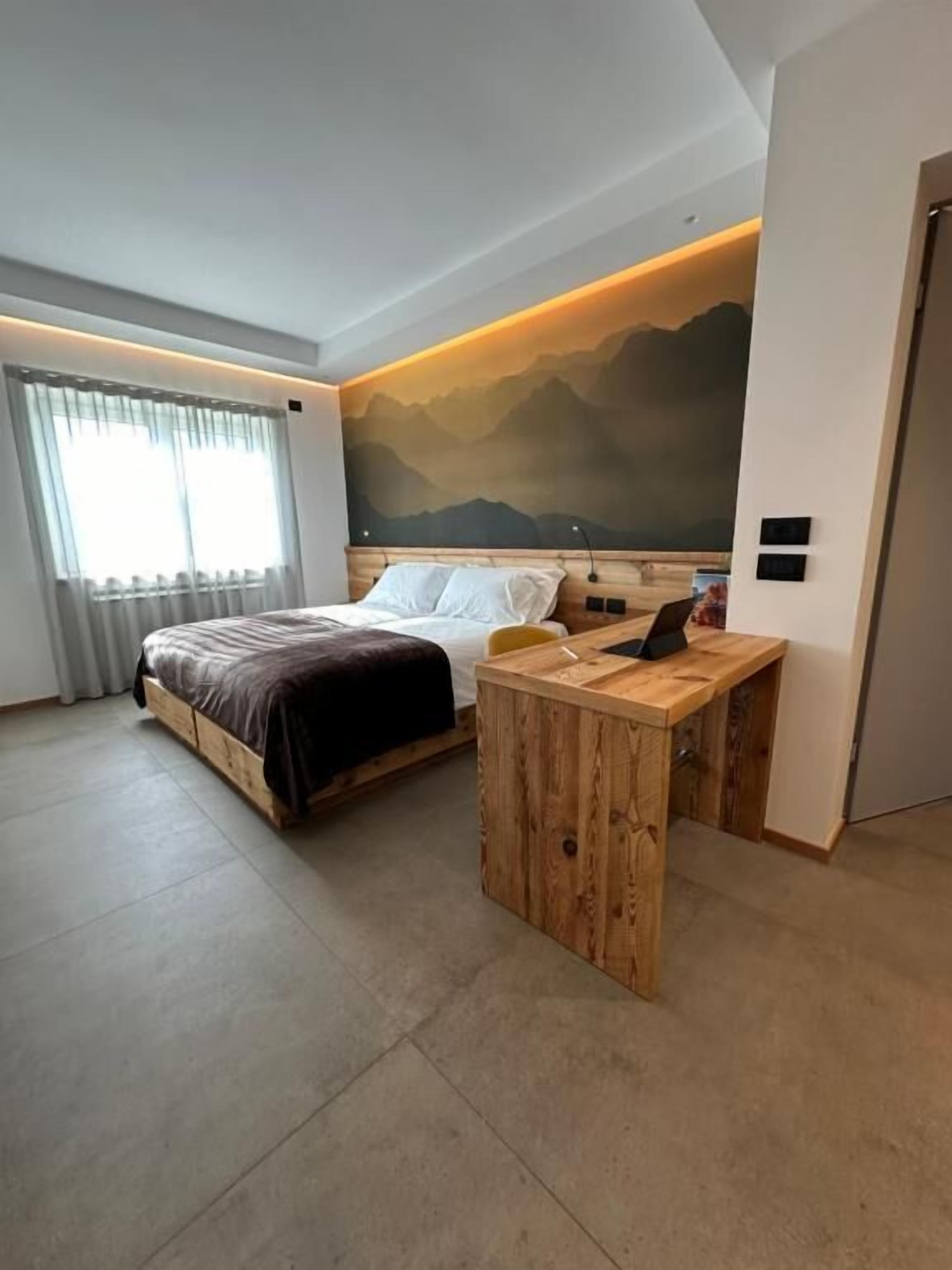 Une chambre d’hôtel moderne avec un lit, un bureau en bois et une fresque représentant une montagne sur le mur.