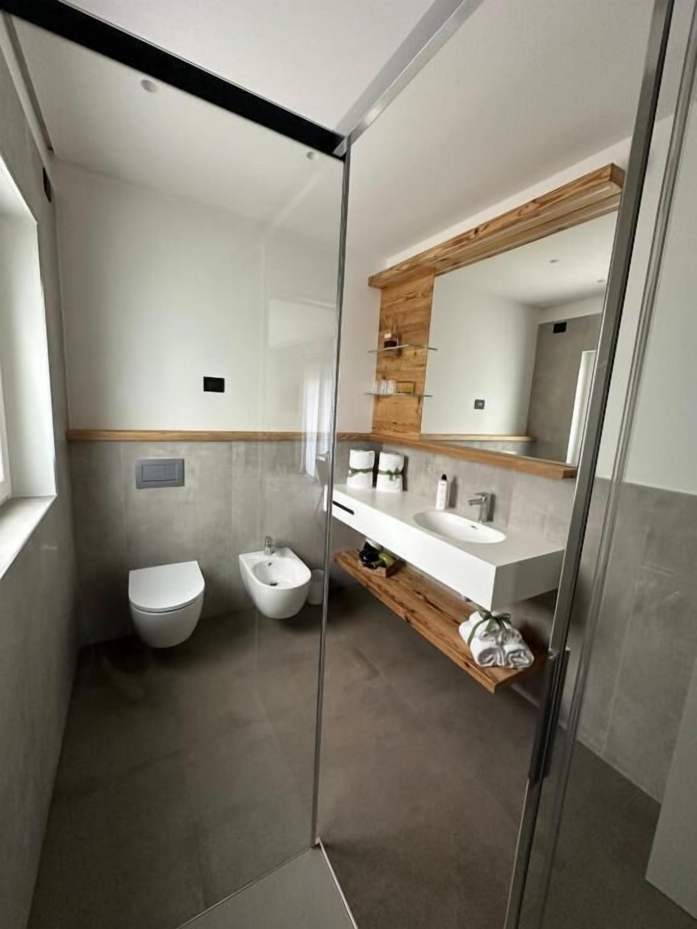 A modern bathroom with a glass shower enclosure, a bidet, a toilet, and a vanity with a mirror.