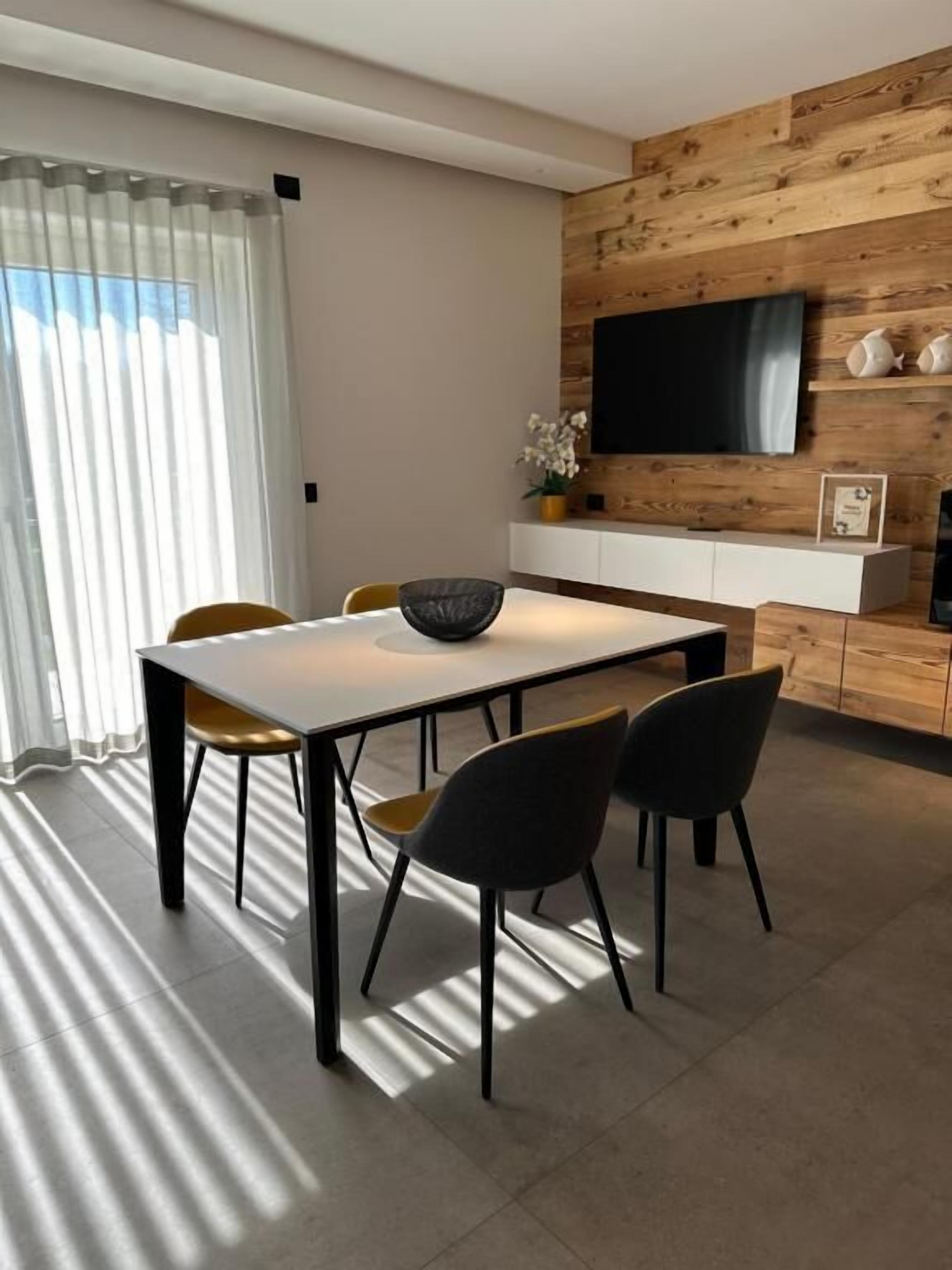 Ein moderner Essbereich mit einem weißen Tisch, schwarzen Stühlen und einer Wandpaneinung aus Holz mit einem Fernseher.