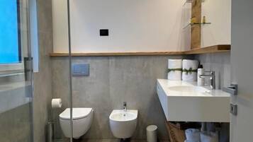 Ein modernes Badezimmer mit einer Duschkabine aus Glas, einem Bidet, einem Waschbecken und einem Holzboden mit Handtüchern.