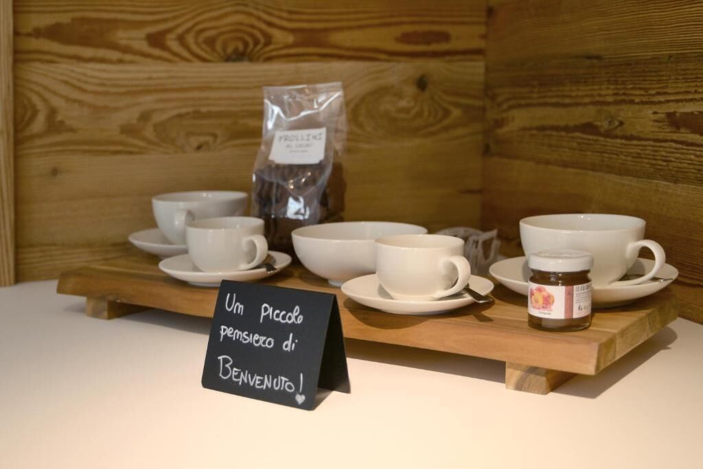 Une collection de tasses et de soucoupes blanches est exposée sur un présentoir en bois, accompagnée d’une pancarte sur laquelle on peut lire : « Un petit geste de bienvenue ! » et d’un pot de miel.