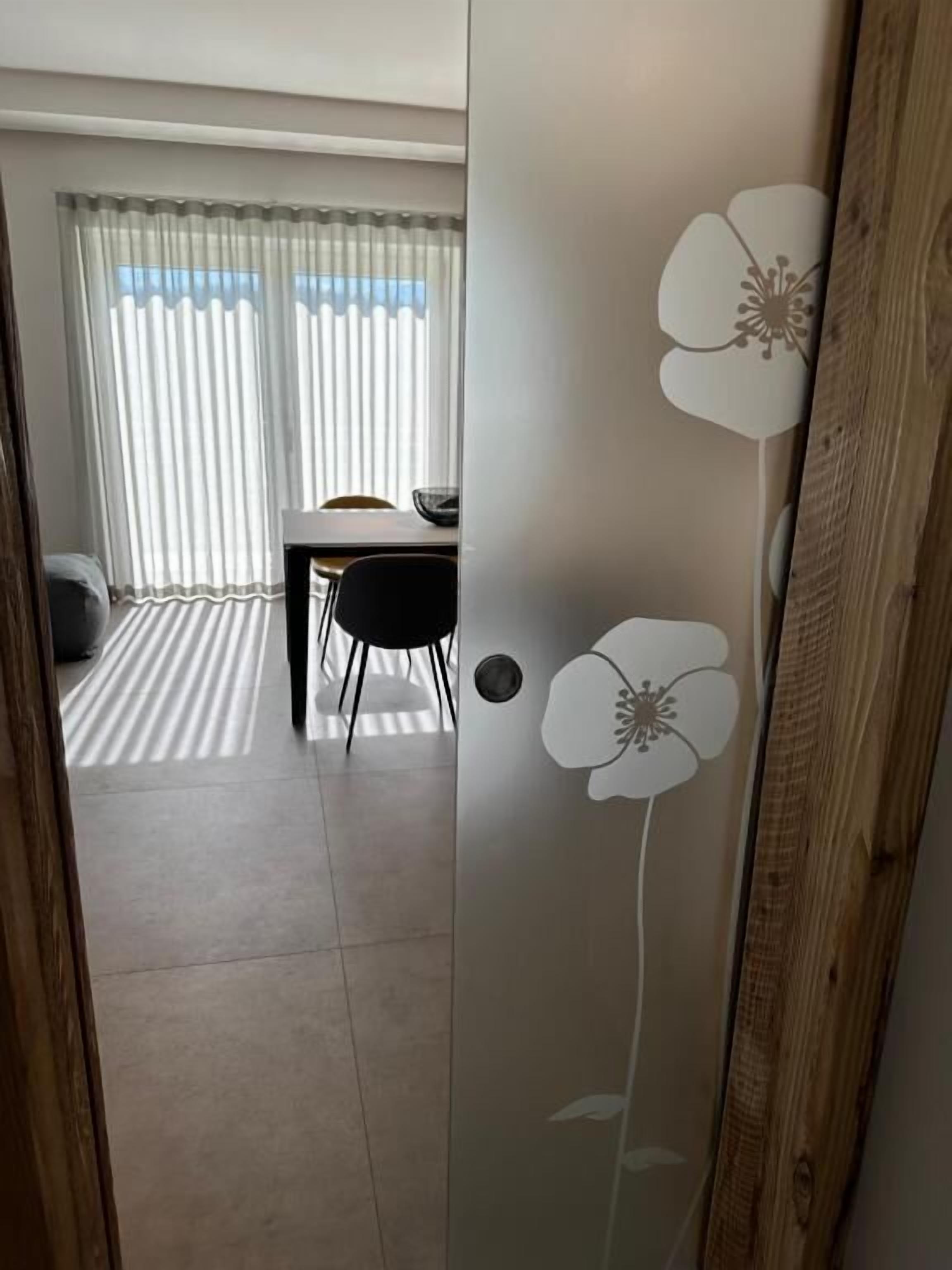 Et værelse med spiseplads, en trædør med blomstermønster og udsigt gennem lette gardiner.