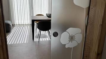 Et værelse med spiseplads, en trædør med blomstermønster og udsigt gennem lette gardiner.