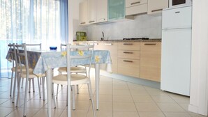 Une cuisine moderne avec des meubles en bois clair, un réfrigérateur blanc et un coin repas comprenant une table et des chaises.