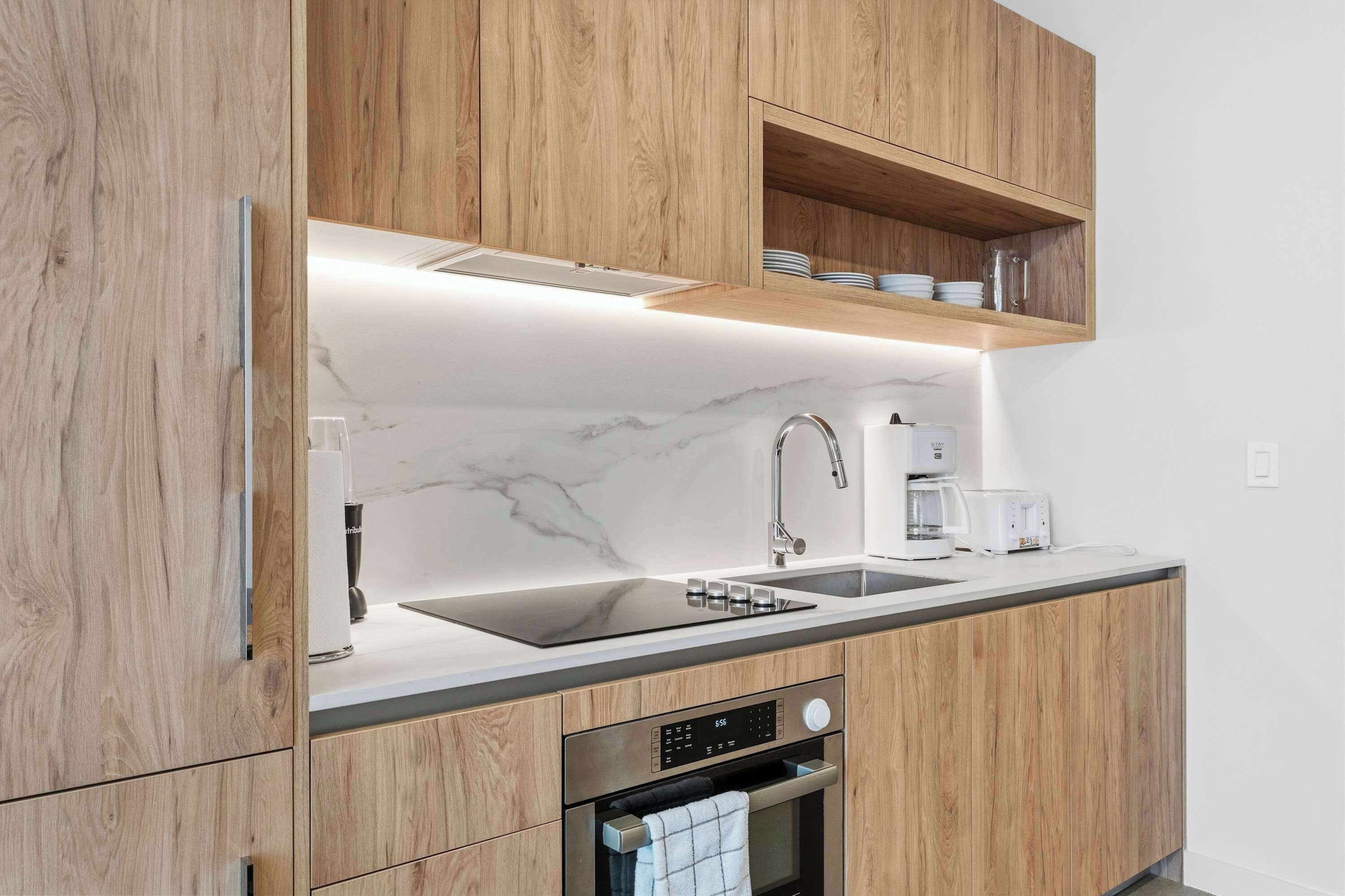 Une cuisine moderne avec des meubles en bois, un plan de travail en marbre, un four encastré et une machine à café.