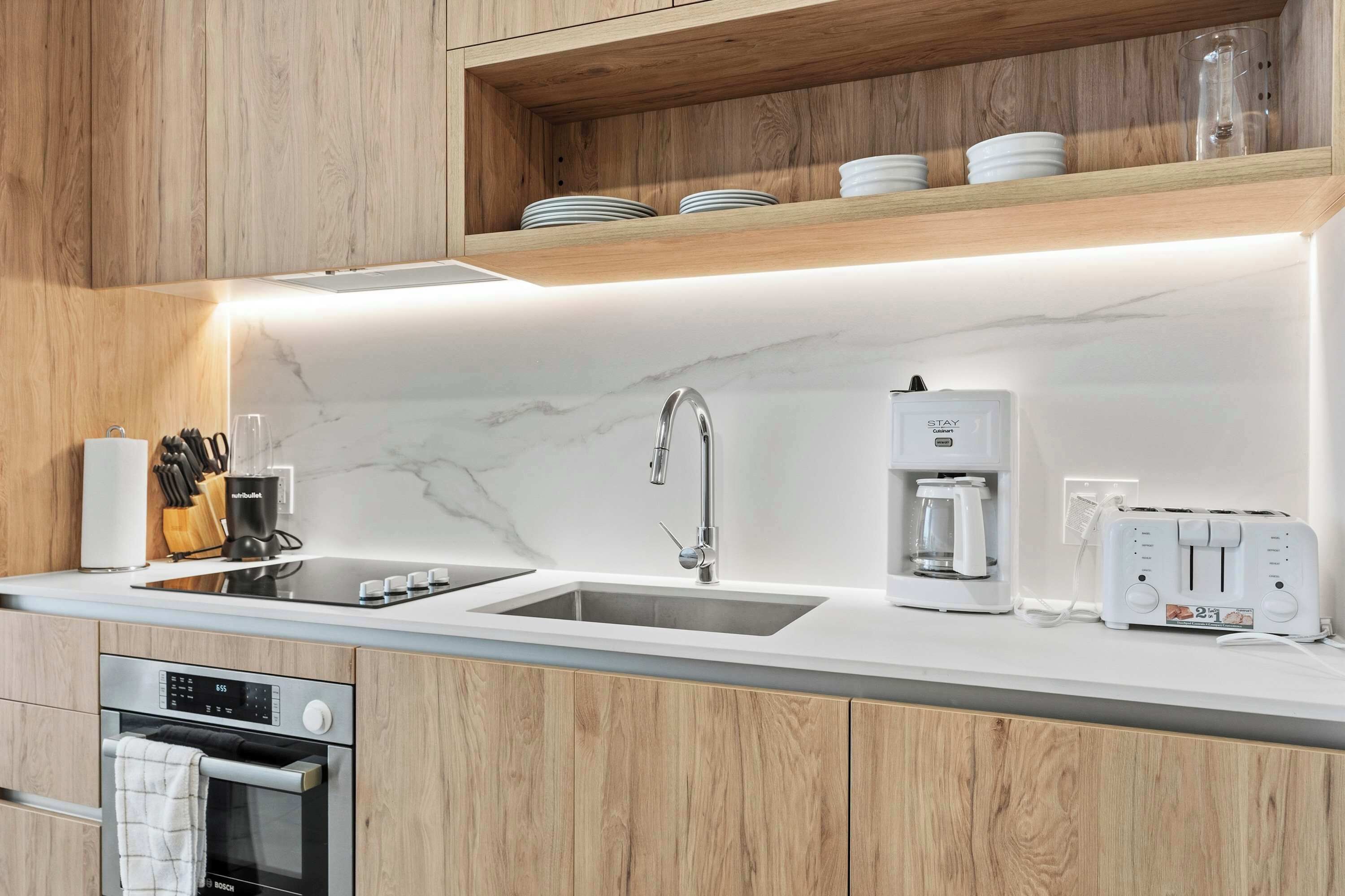 A modern kitchen with wooden cabinets, a marble countertop, a Bosch oven, a sink, a coffee maker, and a toaster.