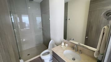 A modern bathroom with a glass-enclosed shower, a toilet, and a sink with a mirror above it.