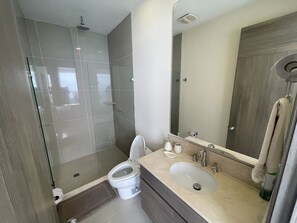 Une salle de bain moderne avec une douche à parois de verre, des toilettes et un lavabo surmonté d’un miroir.