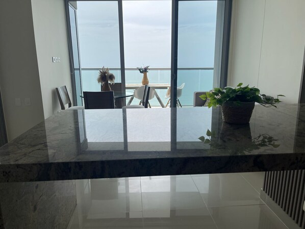 A modern kitchen with a marble countertop, a view of the sea through large windows, and a dining area with a table and chairs. - Edificio Morros City - Bocagrande (Cartagena)