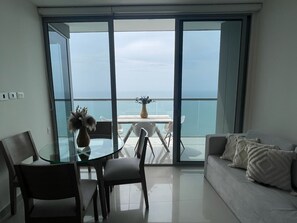 A modern living room with a glass table and chairs, a sofa, and a view of the sea through large sliding doors. - Edificio Morros City - Bocagrande (Cartagena)