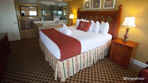 Une chambre d’hôtel avec un grand lit, une salle de bain séparée avec une baignoire, un miroir et une petite table avec une lampe.