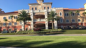 Un hôtel à la façade symétrique, doté de nombreux balcons et orné de palmiers dans le jardin avant.