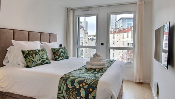 Una habitación de hotel con una cama grande, vistas a edificios a través de la ventana y una lámpara moderna.