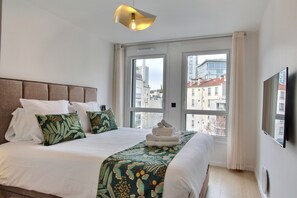 Una habitación de hotel con una cama grande, vistas a edificios a través de la ventana y una lámpara moderna.