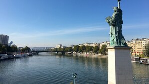 Una estatua de una figura histórica sobre un pedestal, junto a un río con edificios al fondo.