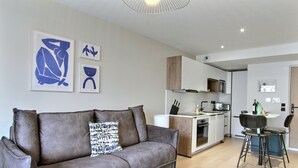 Una sala de estar moderna con un sofá gris, una mesa de centro y una cocina al fondo.