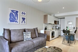 A modern living room with a grey sofa, a coffee table, and a kitchen in the background. - 1 bedroom with A/C in a new building close to the Eiffel Tower (Paris)