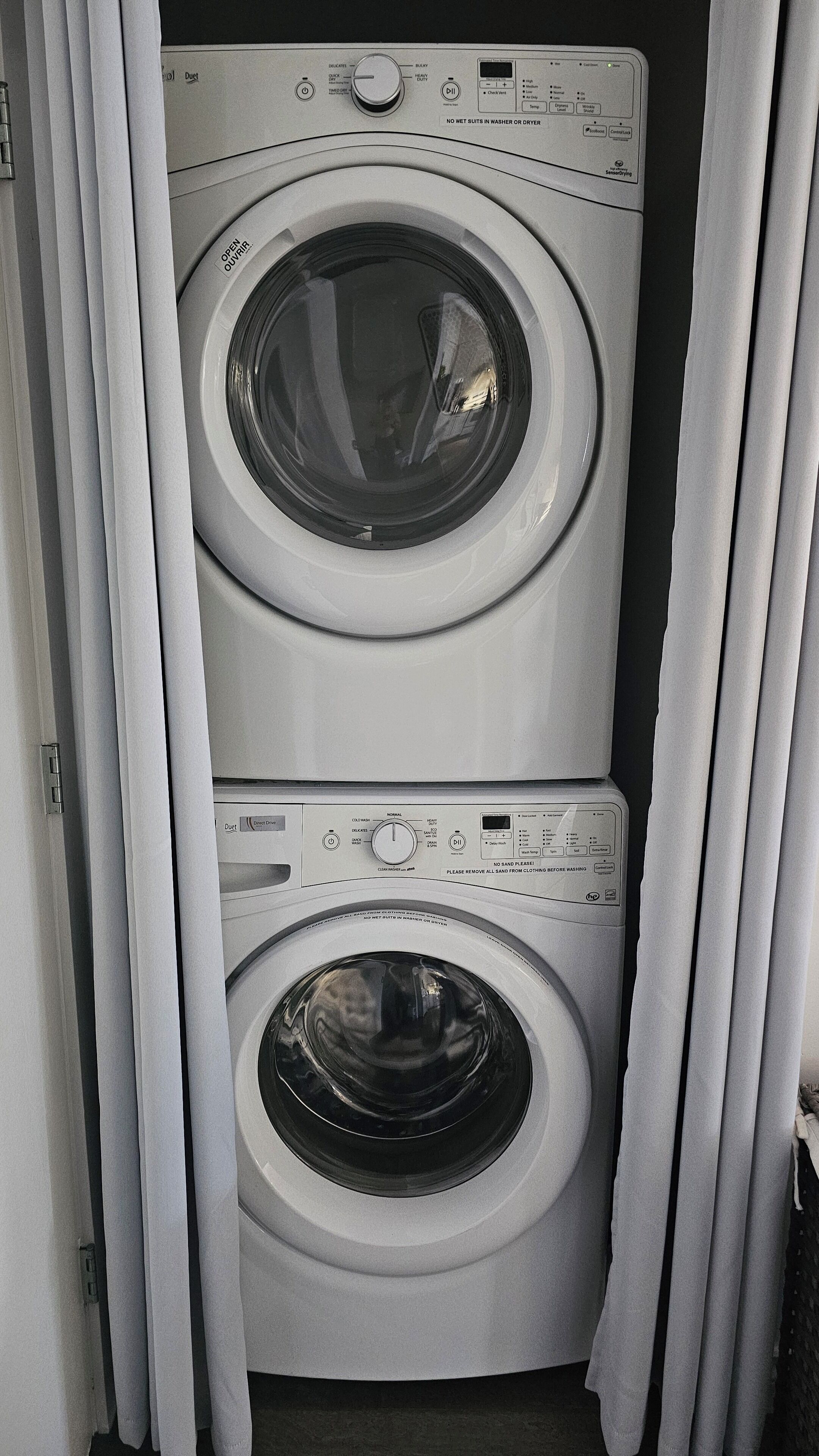 Un appareil compact, combinant lave-linge et sèche-linge, doté de deux portes, avec un panneau de commande situé sur le dessus et une porte en bas.