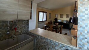 A kitchen with a tiled backsplash, a sink, and cabinets. There is a dining area with a table and chairs in the background. - Central and very relaxing facility (Alezio)