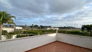 A rooftop terrace with terracotta tiles, white walls, and a view of distant buildings and greenery under a cloudy sky. - Central and very relaxing facility (Alezio)