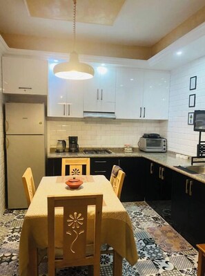 A compact kitchen with white cabinets, a microwave, a coffee maker, and a patterned floor. - Apartment Youssef 5 min walk from the beach (Essaouira)