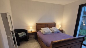 A bedroom with a wooden bed, two bedside tables with lamps, a chair with folded towels, and a large window. - Ground floor room with unlimited access to outdoor spa (Porcaro)