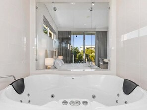 Ein modernes Badezimmer mit einer großen, weißen Badewanne, einer Duschkabine aus Glas und Blick auf einen Balkon mit Gartenmöbeln.