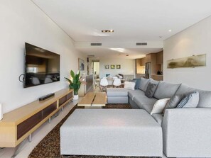 Ein modernes Wohnzimmer mit grauem Sofa, Couchtisch und an der Wand befestigtem Fernseher.