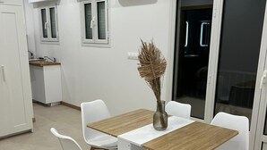 A modern dining area with a wooden table and white chairs, a kitchen in the background, and a large sliding glass door. - HOLLYWOOD RIVIERA (Cannes)