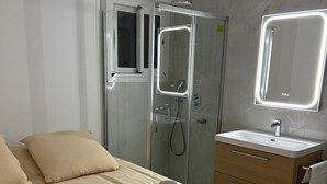 A modern hotel room with a bed, a glass-enclosed shower, a vanity with a mirror, and a towel on the bed. - HOLLYWOOD RIVIERA (Cannes)