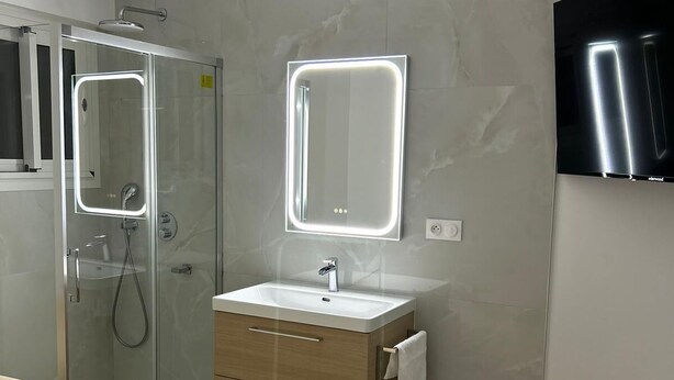 A modern bathroom with a glass-enclosed shower, a vanity with a mirror, and a bed with a rolled towel. - HOLLYWOOD RIVIERA (Cannes)