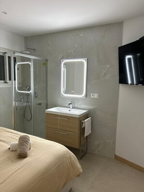 Uma casa de banho moderna com cabine de duche em vidro, espelho sobre a sanita e uma cama com toalha enrolada.