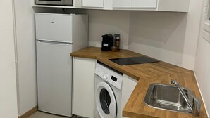 A compact kitchen with white cabinetry, a microwave, a refrigerator, a washing machine, and a wooden countertop with a sink. - HOLLYWOOD RIVIERA (Cannes)