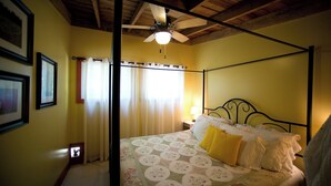 Un dormitorio con cama con dosel, ventilador de techo y ventana con cortinas.