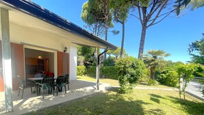 Un patio con tavolo e sedie, una zona relax coperta e vista su un prato curato e alberi.