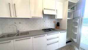 Una cucina con mobili bianchi, un lavello in acciaio inossidabile, un piano cottura a gas e un frigorifero.