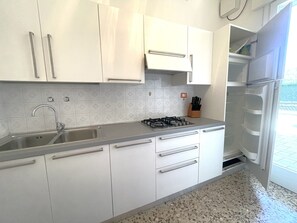 Eine Küche mit weißen Schränken, einer Edelstahl-Spüle, einem Gasherd und einem Kühlschrank.