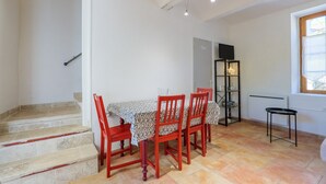 Un comedor con mesa, sillas, una escalera, un radiador y una ventana.