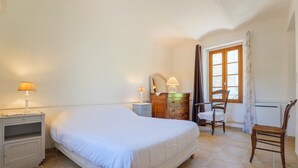 Un dormitorio con cama, mesitas de noche, cómoda, silla y ventana.