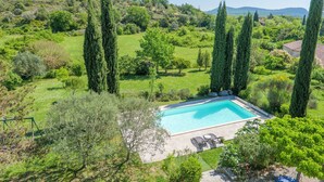 Piscina con zona de patio, rodeada de vegetación y cipreses.