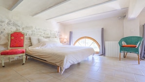 Ein Schlafzimmer mit einem Bett, einem Sessel, einer Steinsäule und einem Fenster.