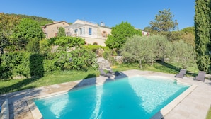 Ein Pool mit Liegestühlen, ein Steinhaus und umliegendes Grün.
