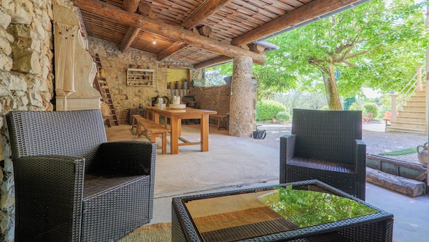 Ein Außenbereich mit einer Terrasse, Korbmöbeln, einer Steinwand und einer Holzbalkendecke.
